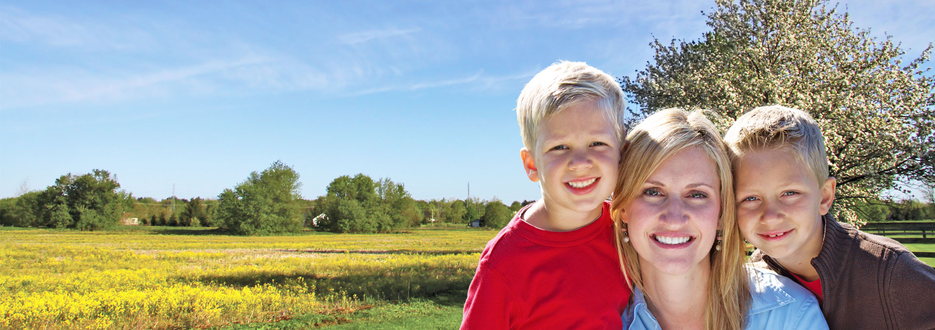 Mother and two young sons hugging and smiling with a farm in the background