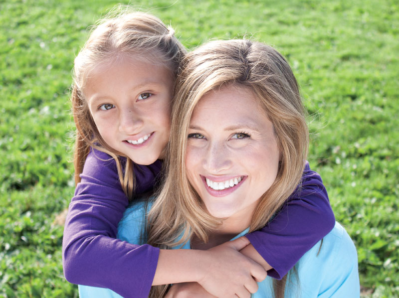 Young girl hugging a woman's shoulders both are smiling