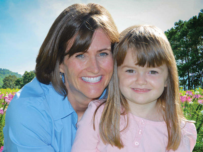 Woman hugging young girl around waist both are smiling and standing in a field of flowers